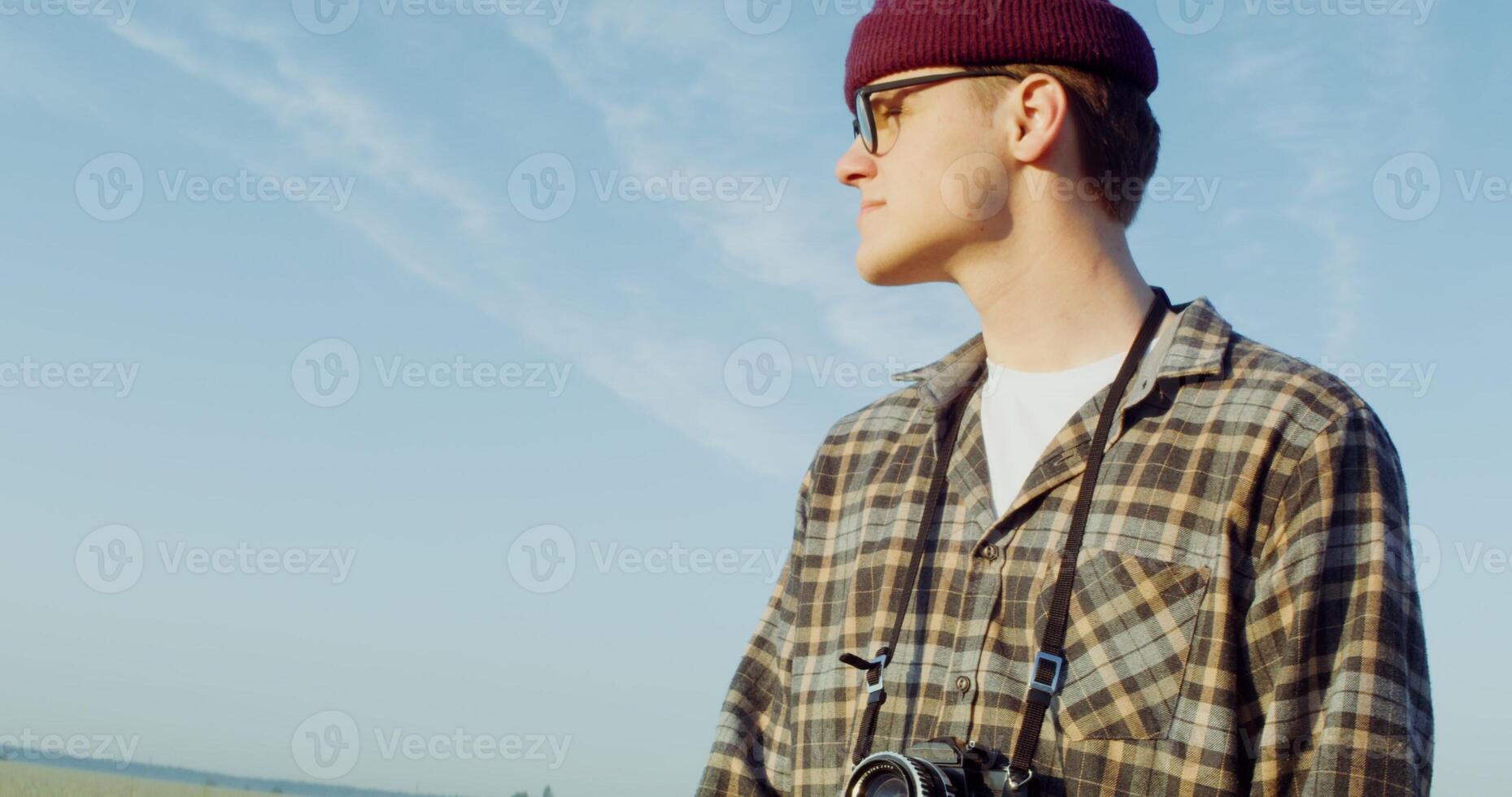A young stylishly dressed man with a camera hanging around his neck stands in the middle of a gravel road with a bicycle in his hands and admires the fields around him. 4k , red komodo - camera photo