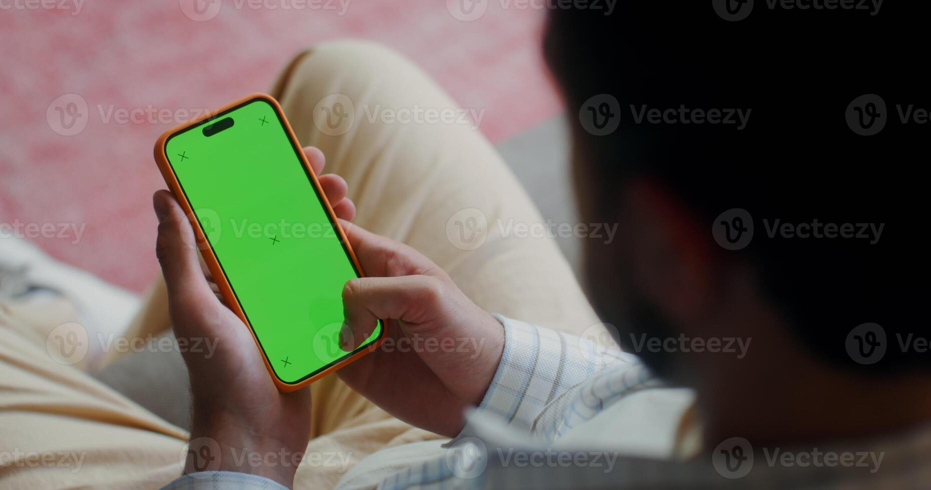 A man in casual clothes scroll the green screen of a mobile phone while sitting on the couch at home. Top view, no face, close-up of a man's hands - scroll photo