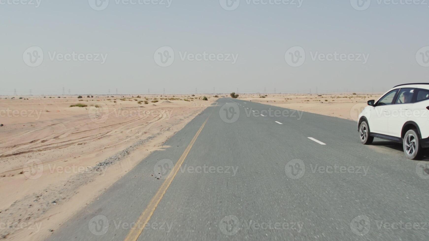 A drone view of a car driving along a road through a desert with sparse vegetation among the sands - sparse photo
