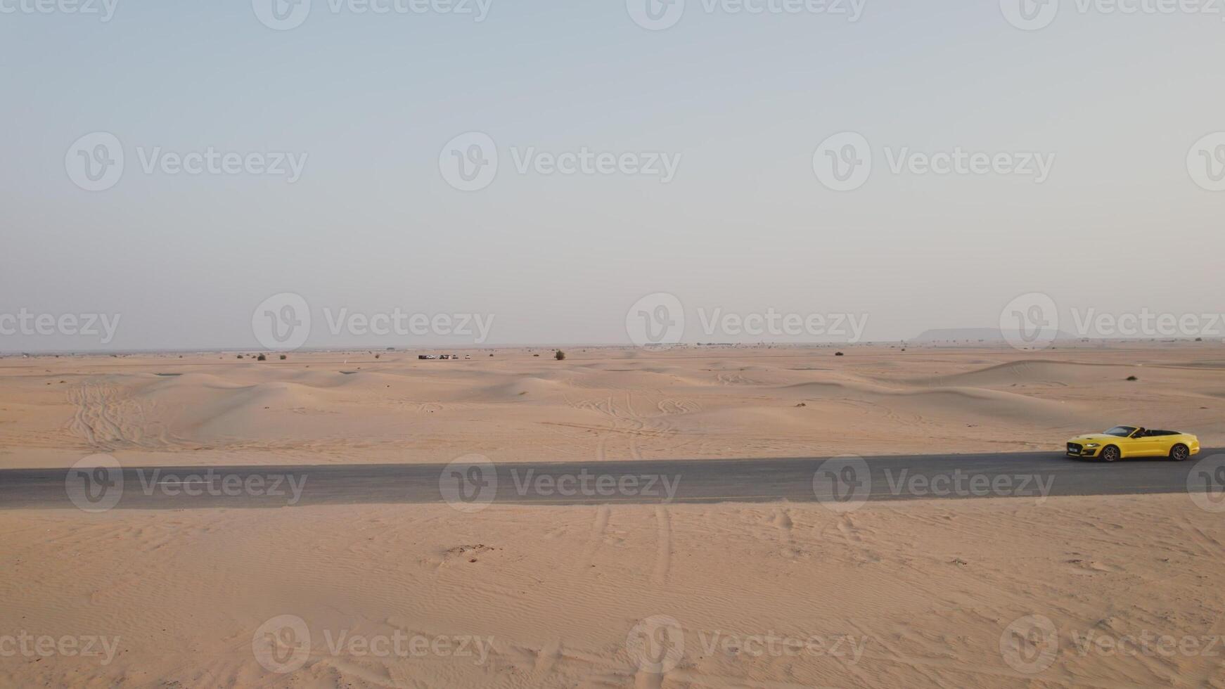 The drone flies parallel to a yellow car driving along the road among the desert sands photo