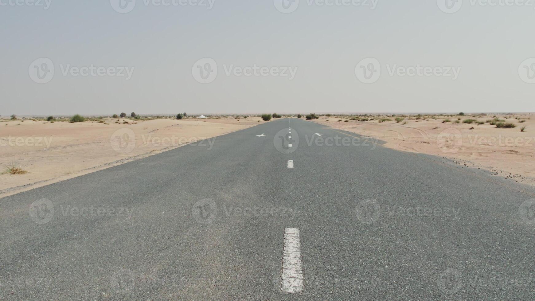A drone view of a car driving along a road through a desert with sparse vegetation among the sands photo