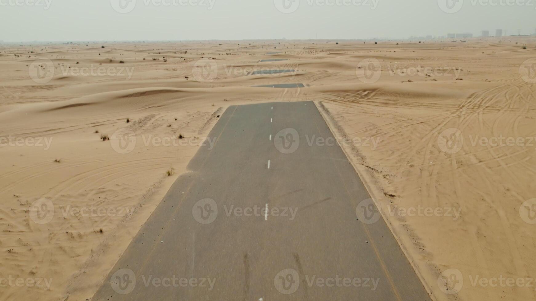 The drone flies over a modern paved road in the middle of a desert with sand dunes covering it photo