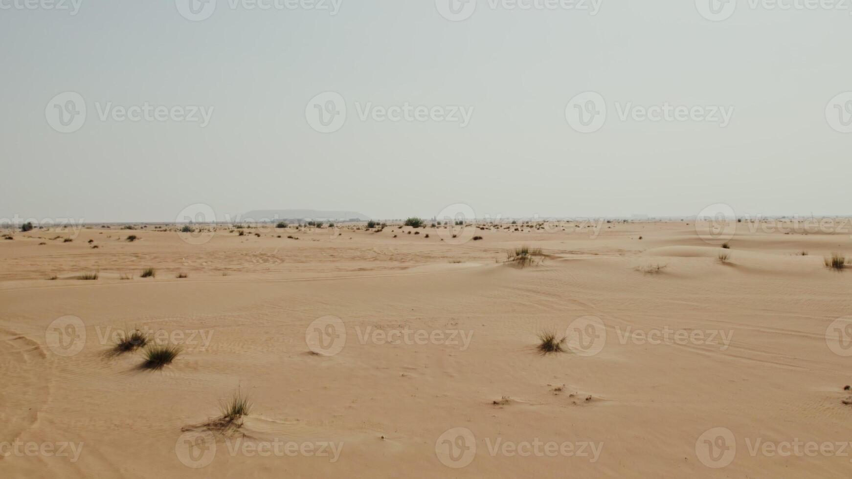 The drone flies over a desert with sparse green vegetation and debris lying among the sand photo
