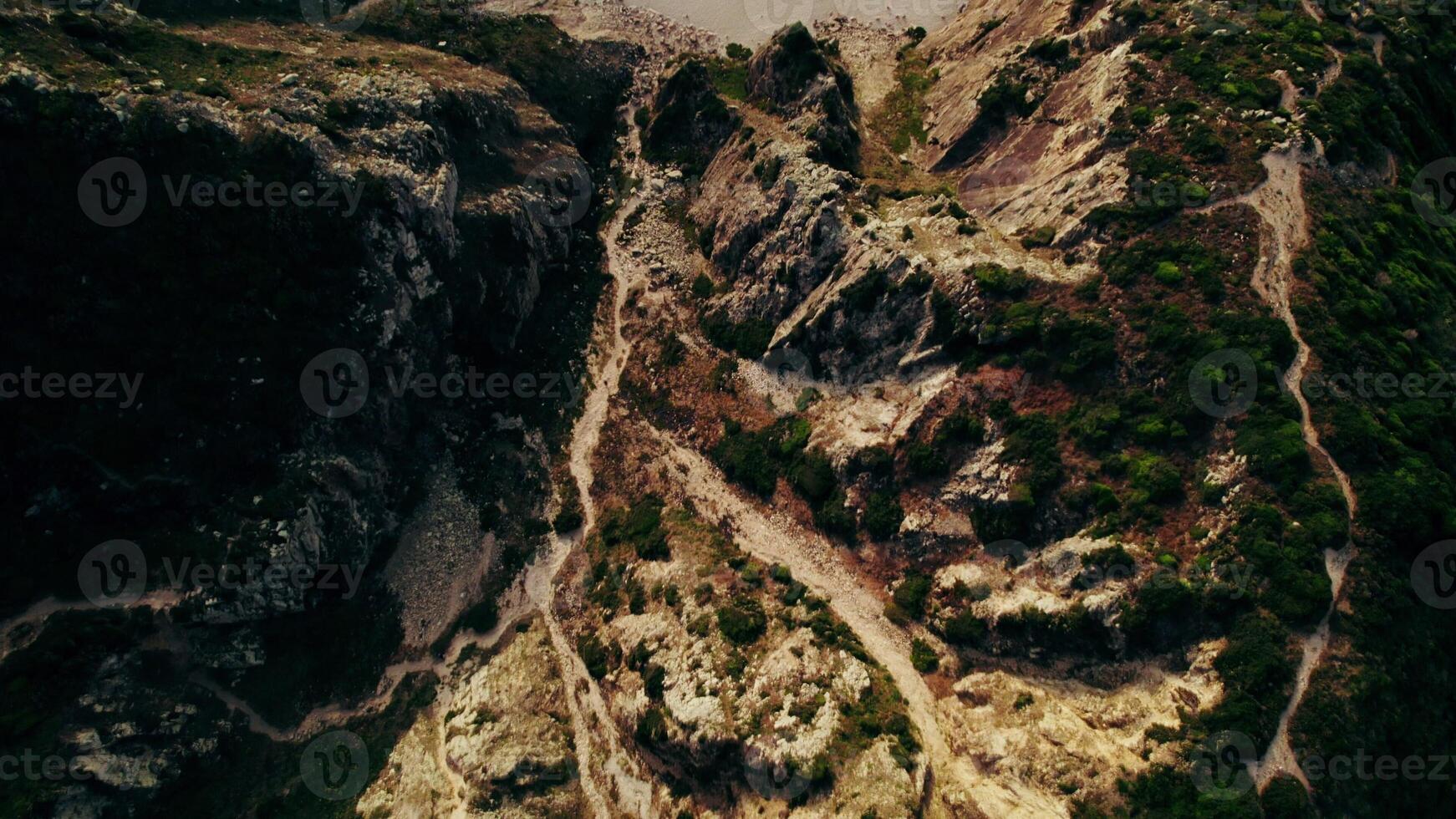 The drone flies from the top of a mountain overgrown with grass towards the sea, with a sandy beach between the rocks photo
