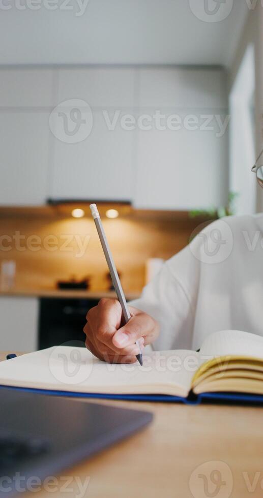 The girl does her homework at home, she uses a laptop and makes notes in a notebook while sitting at the kitchen table. Close-up of a girl's hands photo