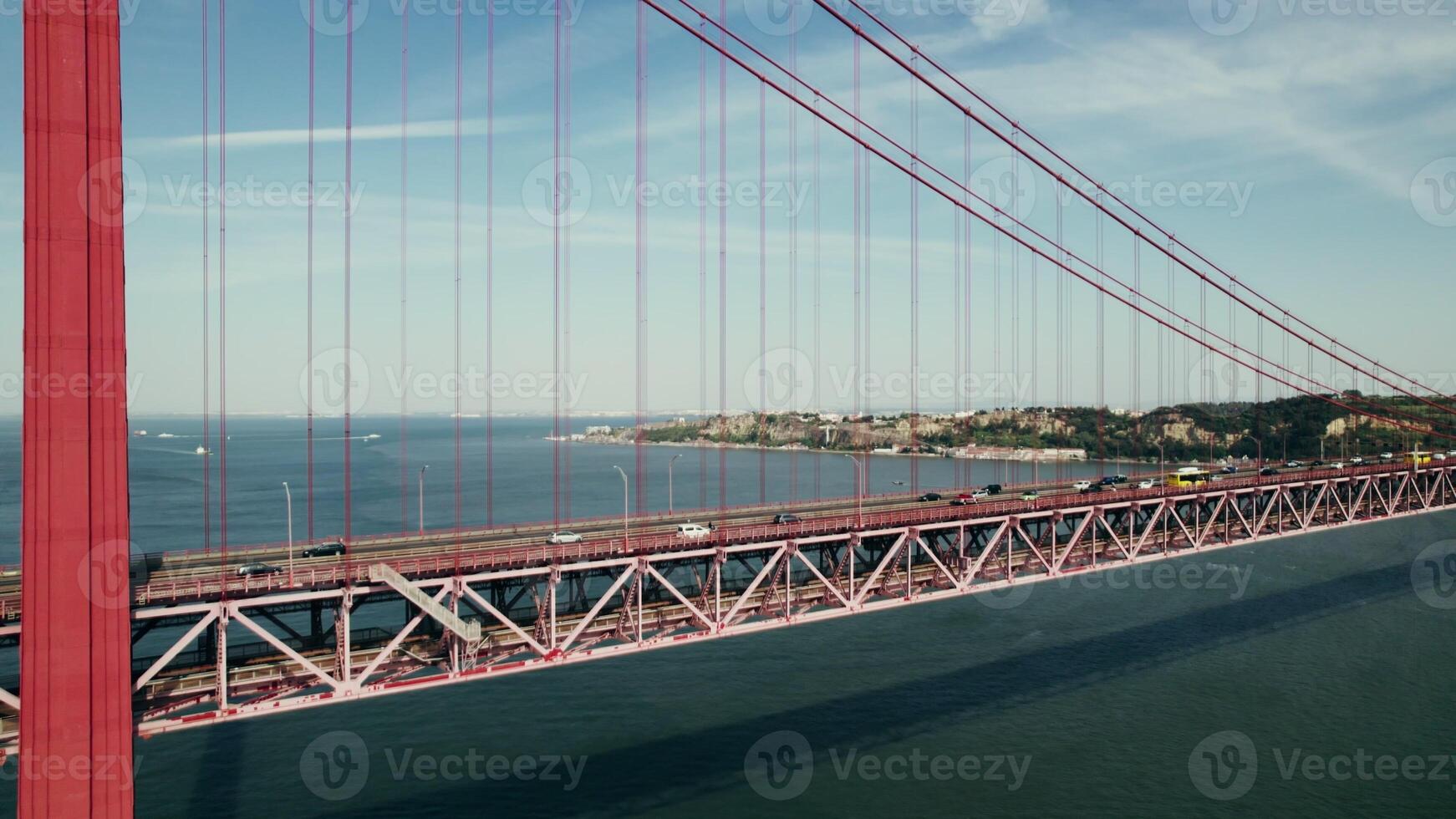 The drone flies near the red suspension bridge over the river, with cars passing on it - passing photo
