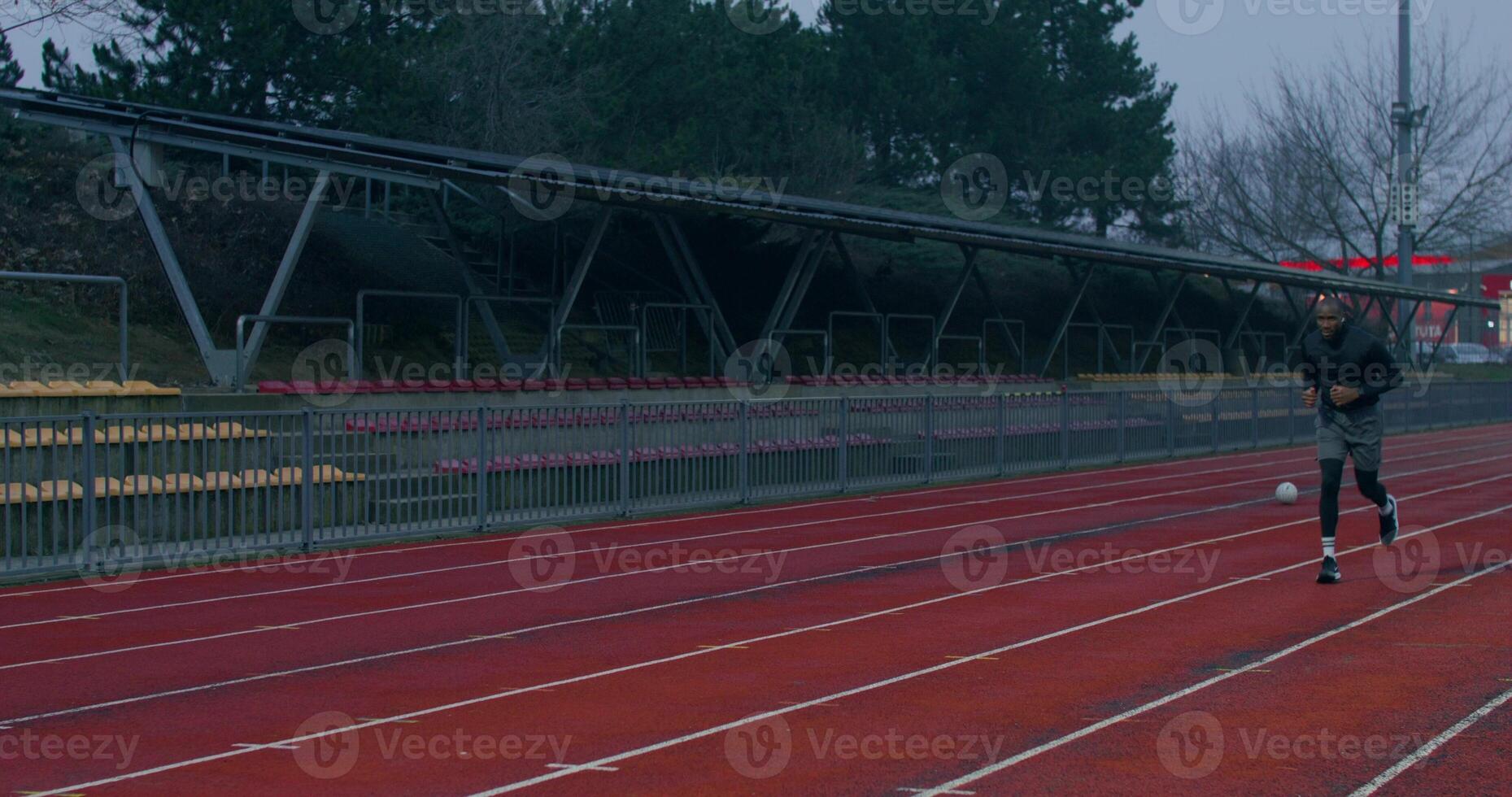 A man in sports clothes runs around the stadium on a cold day alone. He looks at his wristwatch. photo