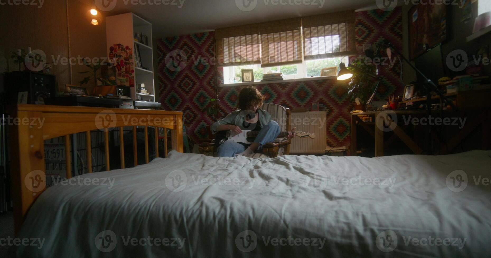 A young woman plays the guitar sitting in an armchair at home with a depressed look. Bedroom in the basement - armchair photo