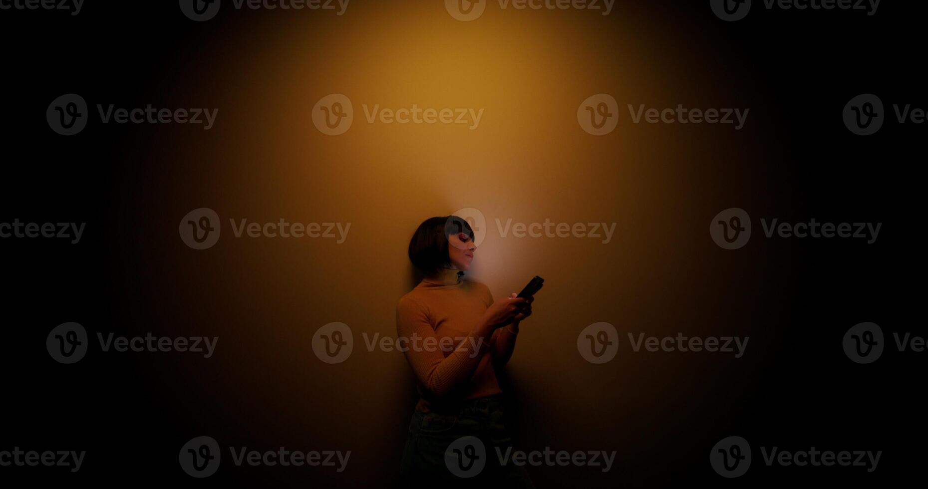 A woman in a wig uses a mobile phone, leaning against the wall in the orange backlight in the studio - orange photo