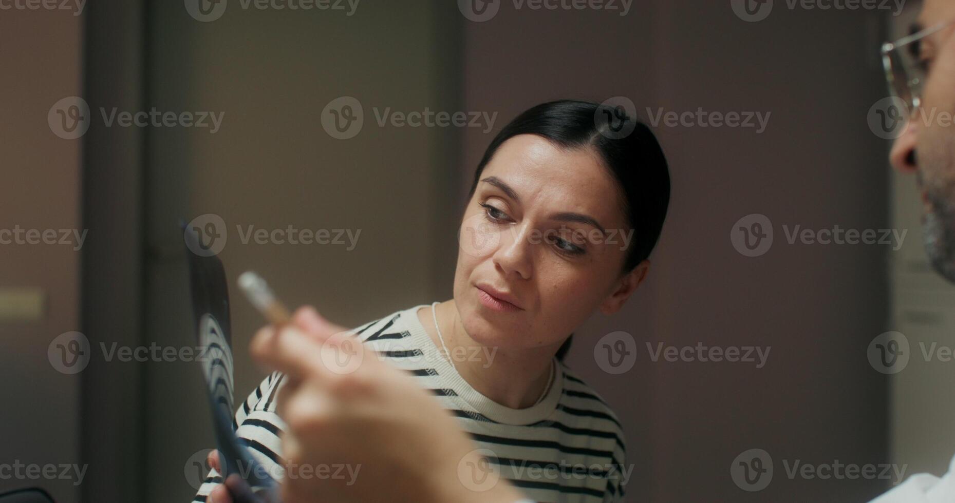 A doctor in a white coat and a female patient view an X-ray sitting at a table in a medical office at the clinic - medical photo