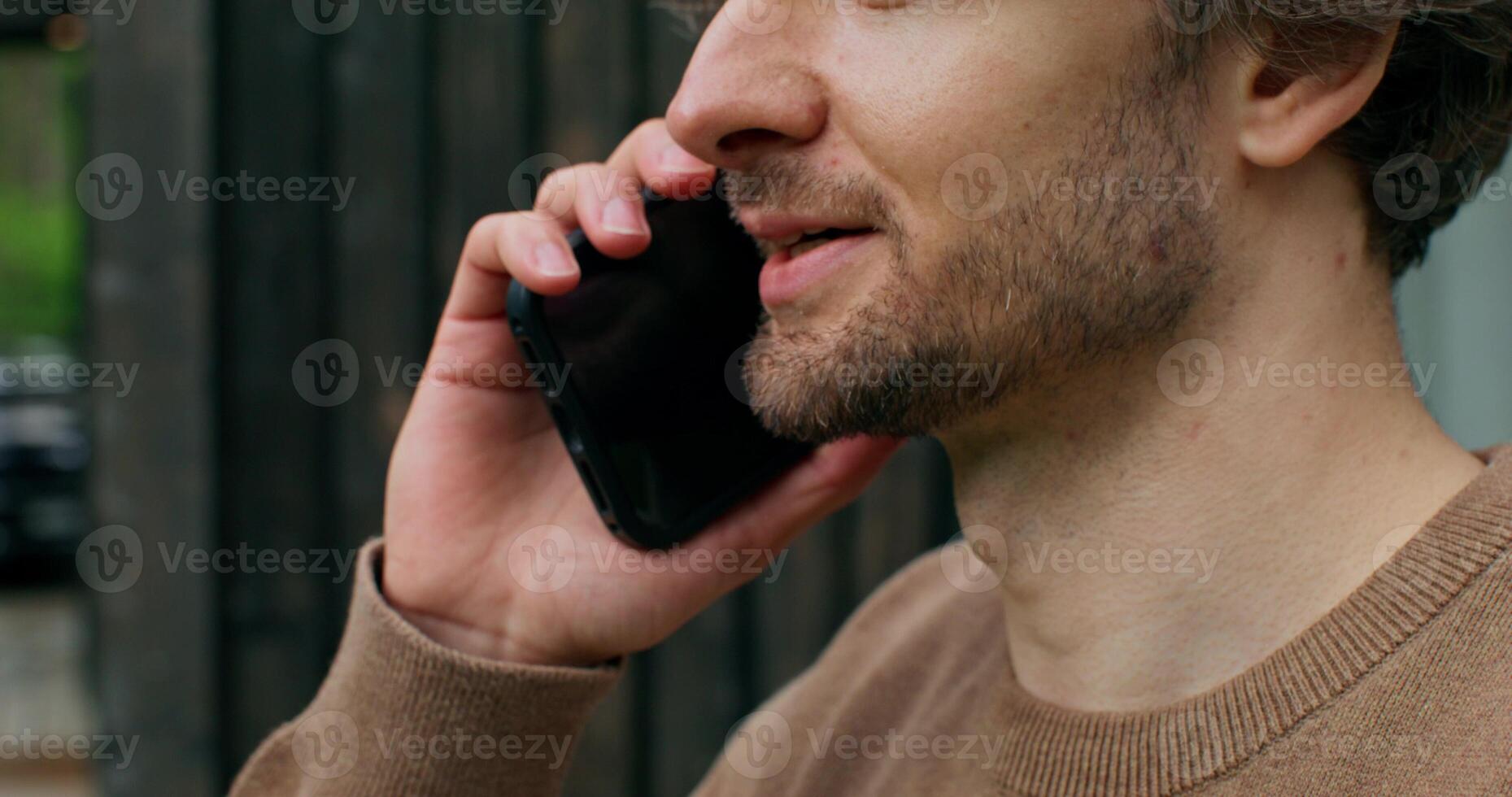 A man in casual clothes is talking on a mobile phone standing on the terrace of a stylish cottage on a summer day. Close-up of his face photo