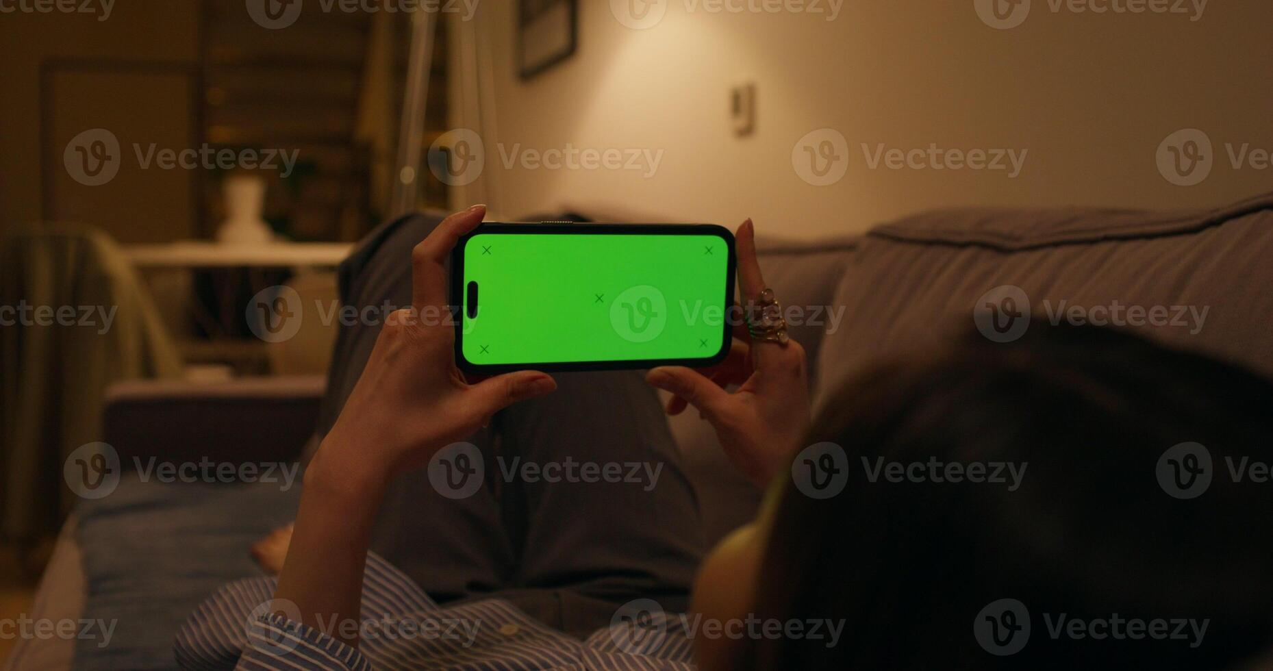A woman uses a mobile phone with a green screen lying on the couch at home, dimmed evening light - evening photo