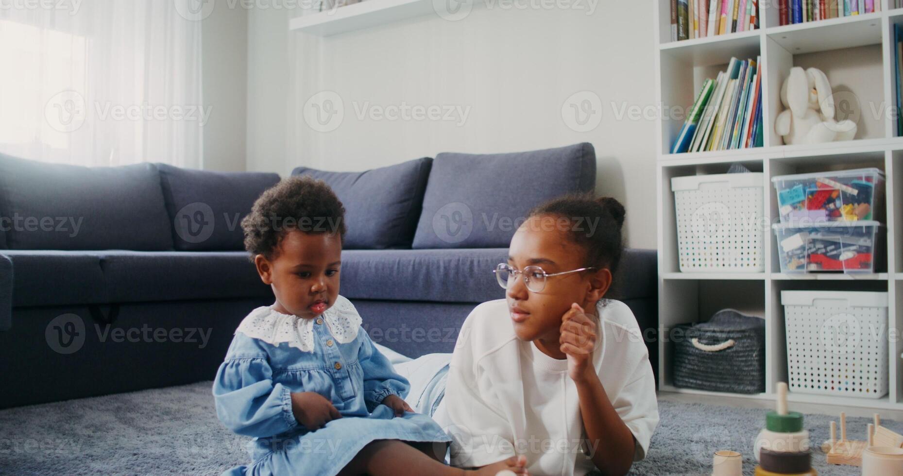 A teenager and a baby girl of African-American appearance watch cartoons on a tablet while sitting on the floor at home - cartoons photo