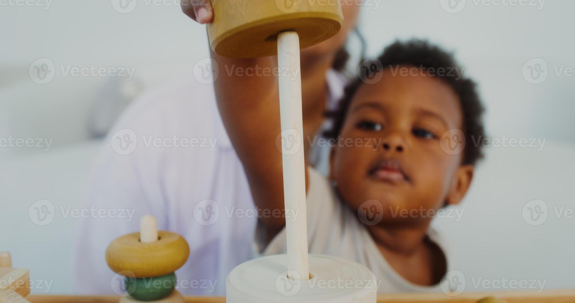Mom and daughter of African-American appearance play with wooden toys sitting near the table in a white room photo