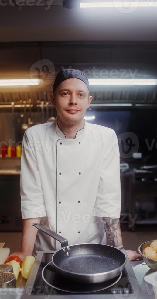 A man in a chef's uniform smiles while looking at the camera standing in the restaurant kitchen photo