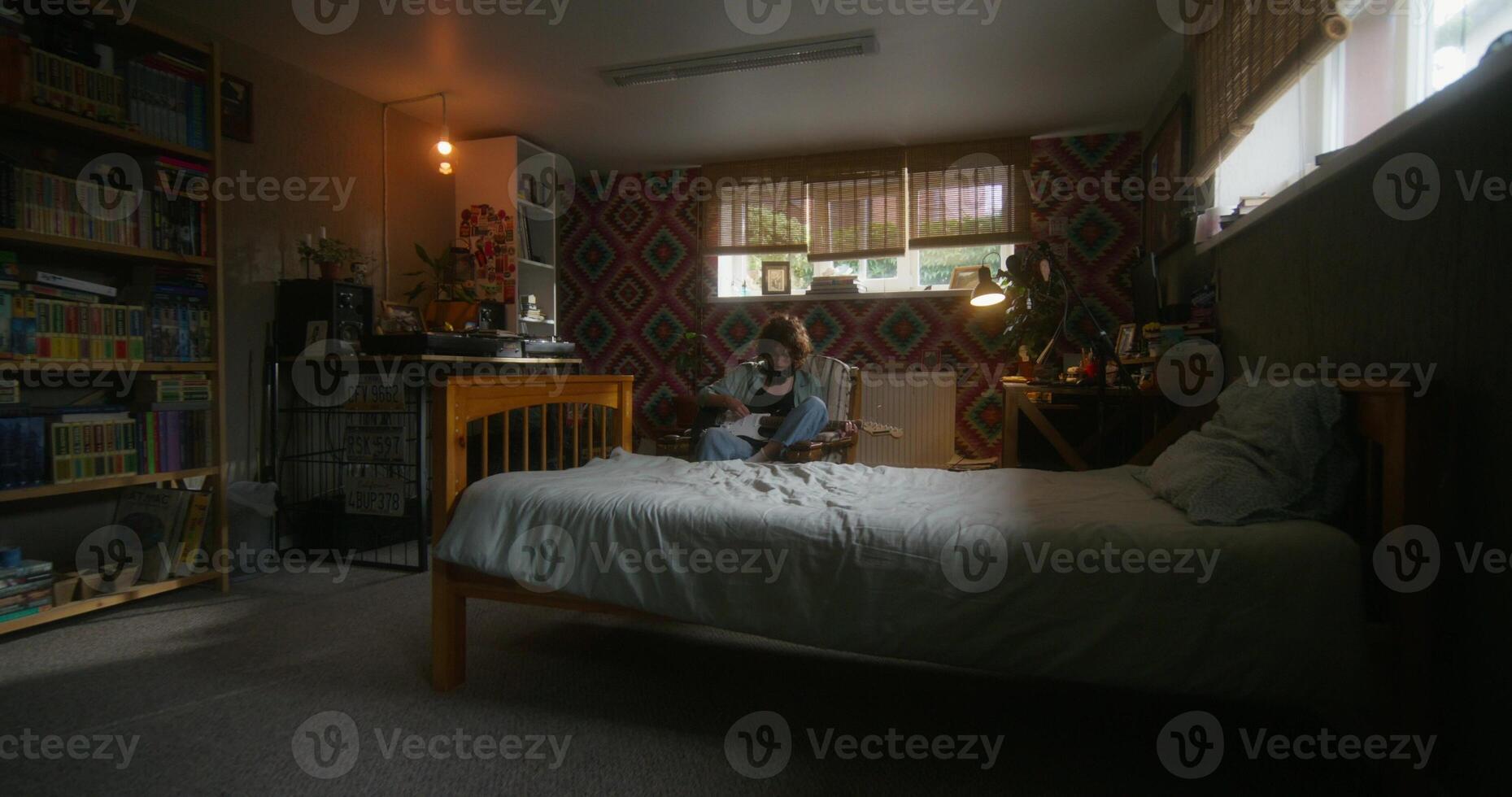 A young woman plays the guitar sitting in an armchair at home with a depressed look. Bedroom in the basement - depressed photo