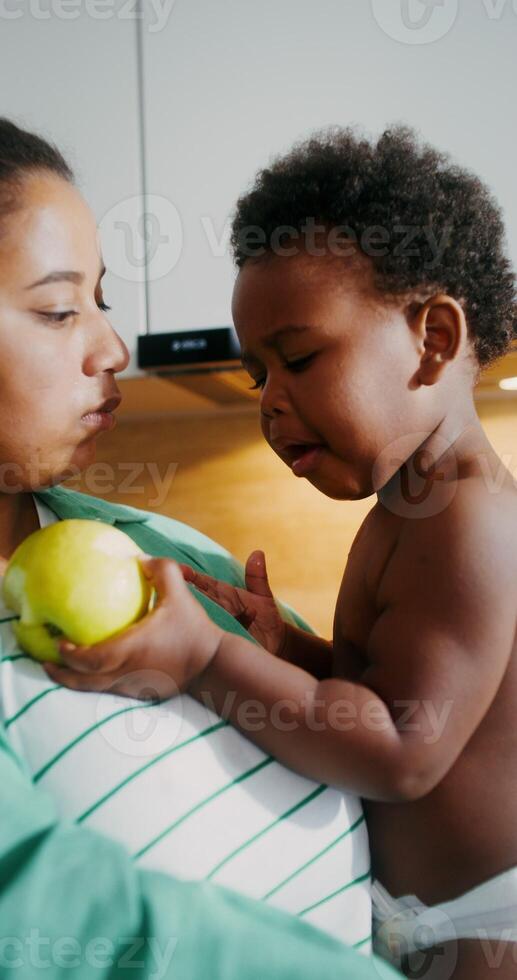 A little African American girl is crying sitting in her mother's arms with an apple in her hand photo