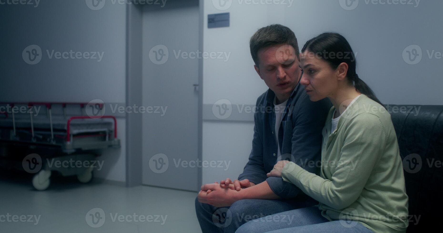 Concerned patient's relatives are waiting sitting on the couch in the hospital corridor. The husband hugs and supports his wife - waiting photo