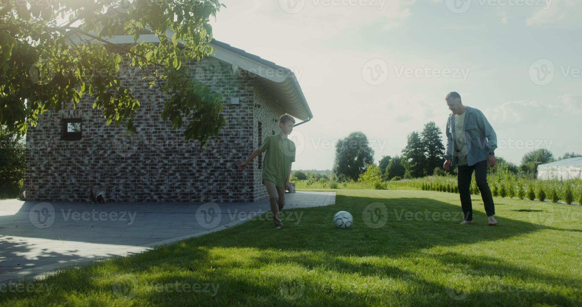 A boy plays soccer with his dad on the backyard lawn on a summer day photo