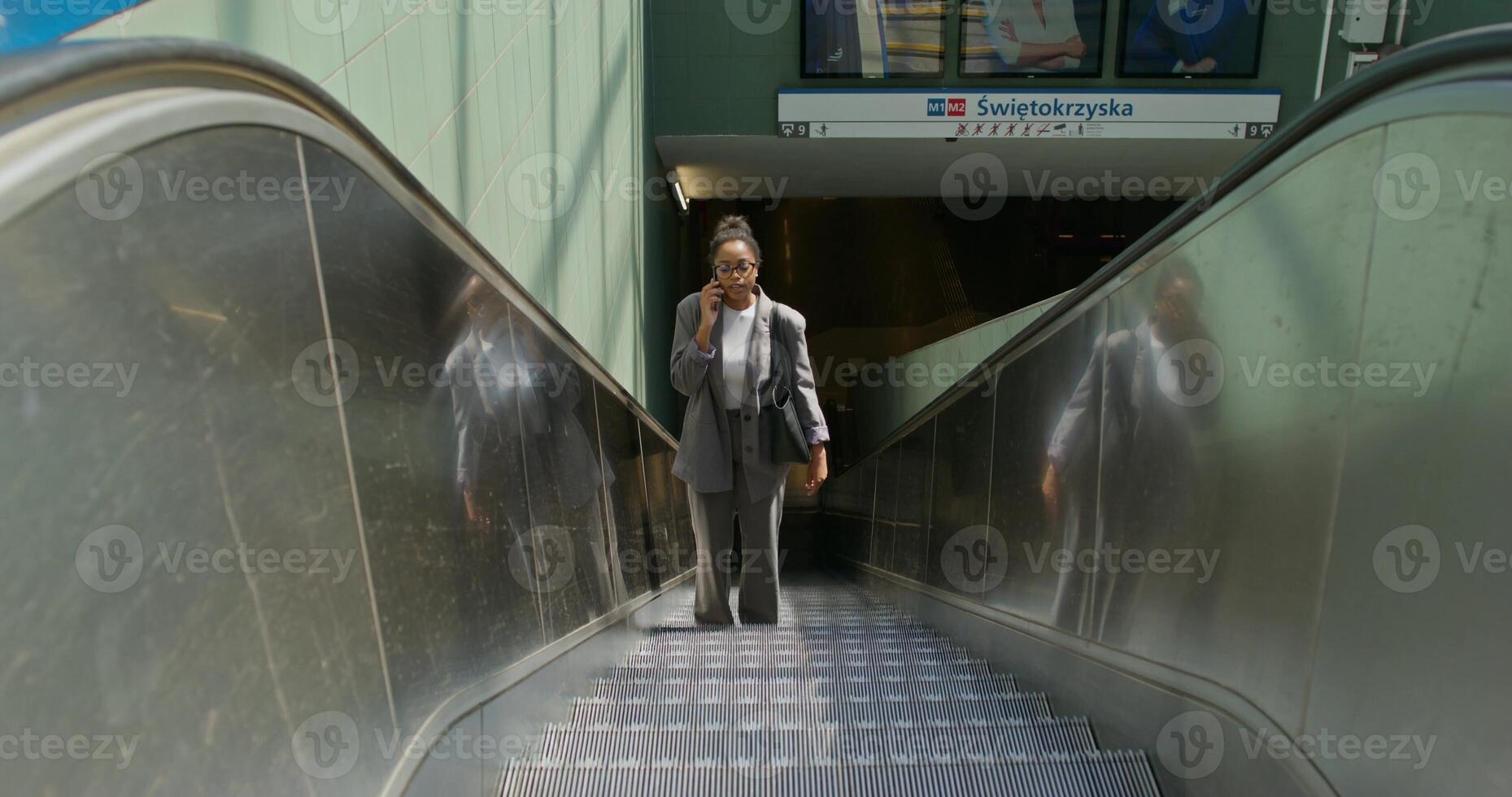A woman in formal clothes is talking on a mobile phone. She rides the escalator coming up from the subway station - mobile photo