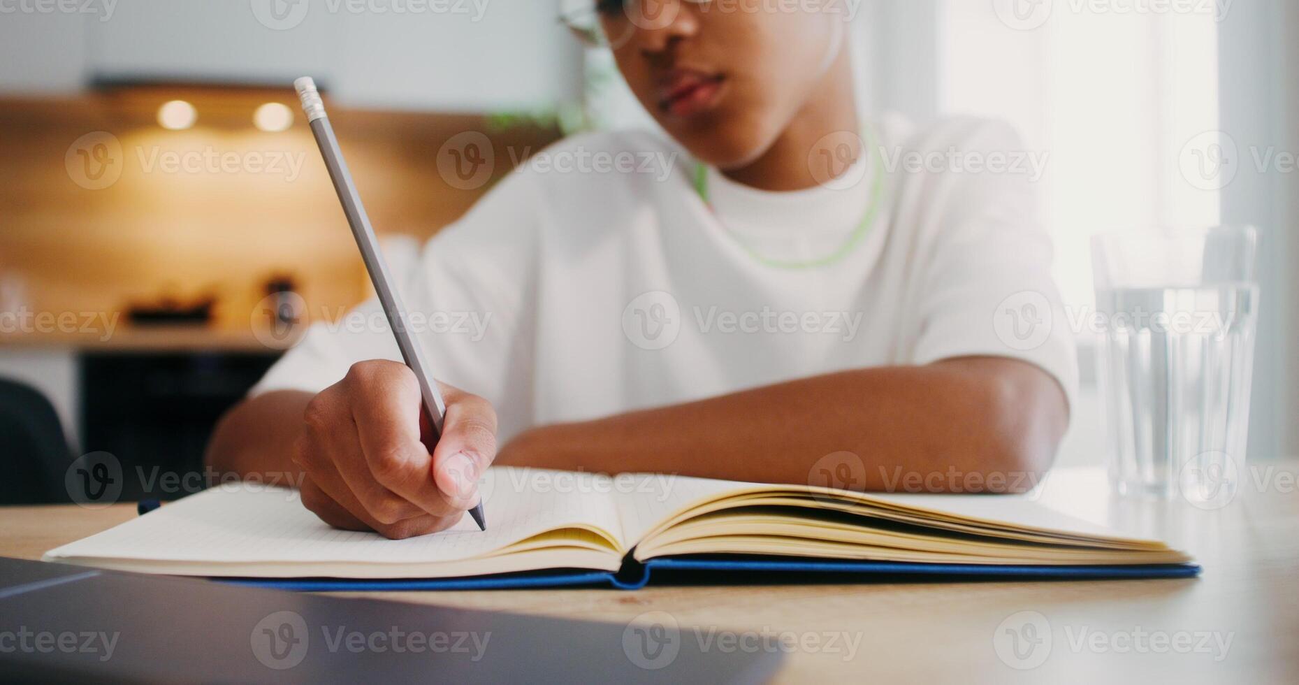 The girl does her homework at home, she uses a laptop and makes notes in a notebook while sitting at the kitchen table. Close-up of a girl's hands - sitting photo