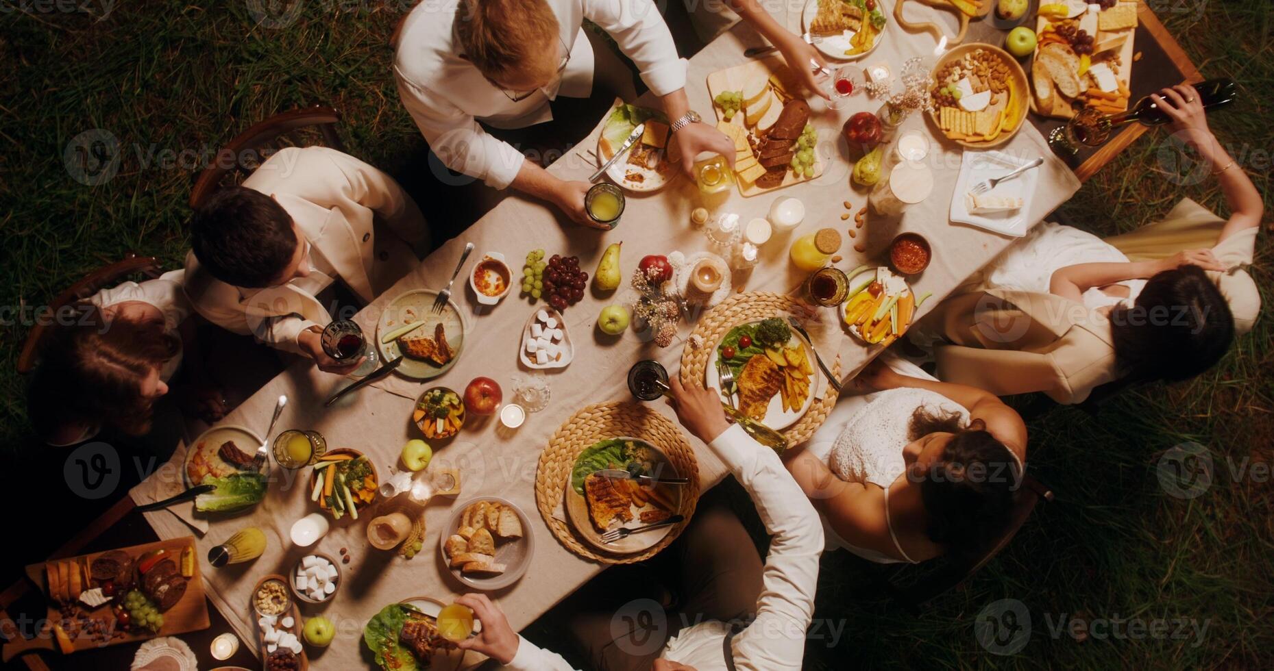 Guests clink glasses sitting at the beautifully served festive table. Top view, outdoor feast - sitting photo