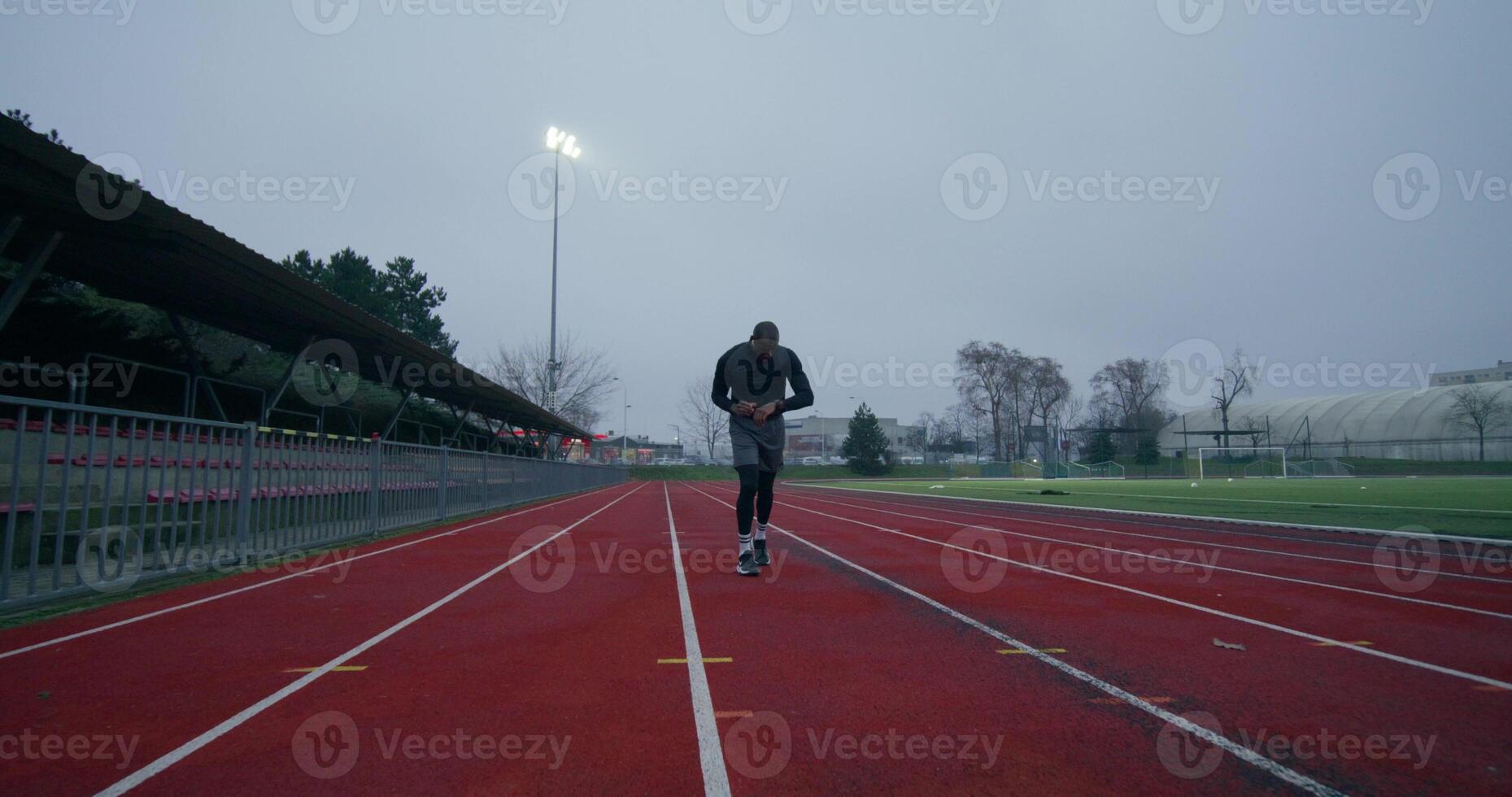 A man in sports clothes runs around the stadium on a cold day alone. He looks at his wristwatch. - around photo