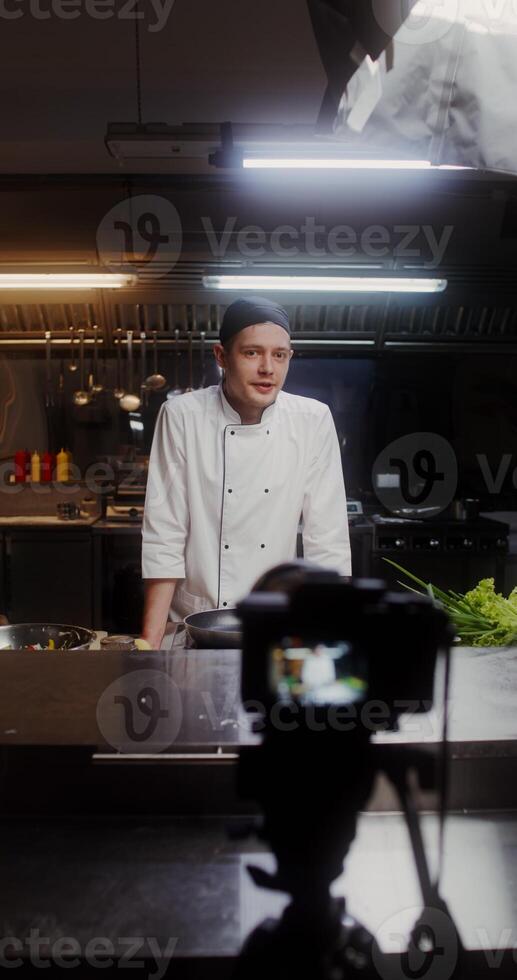 A man in a chef's uniform records the cooking process on , standing near a frying pan in the kitchen of a restaurant photo