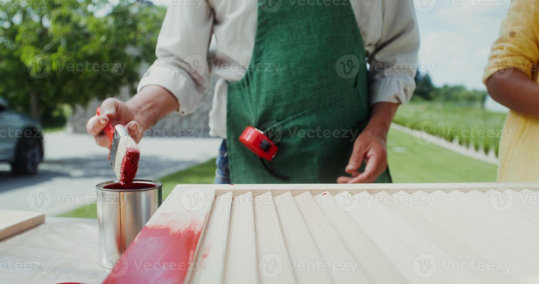 A man in an apron and a boy paint the door with red paint while standing in the backyard. Close-up of hands, no face - standing photo
