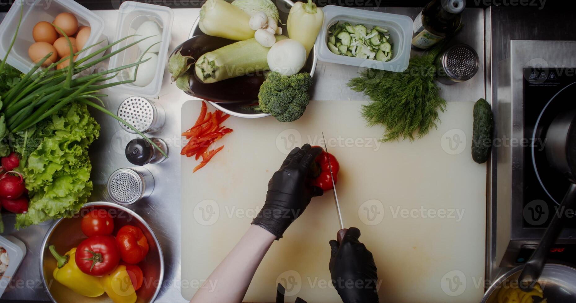 A woman in disposable black gloves cuts peppers standing near a table full of vegetables, close-up of her hands, top view - peppers photo