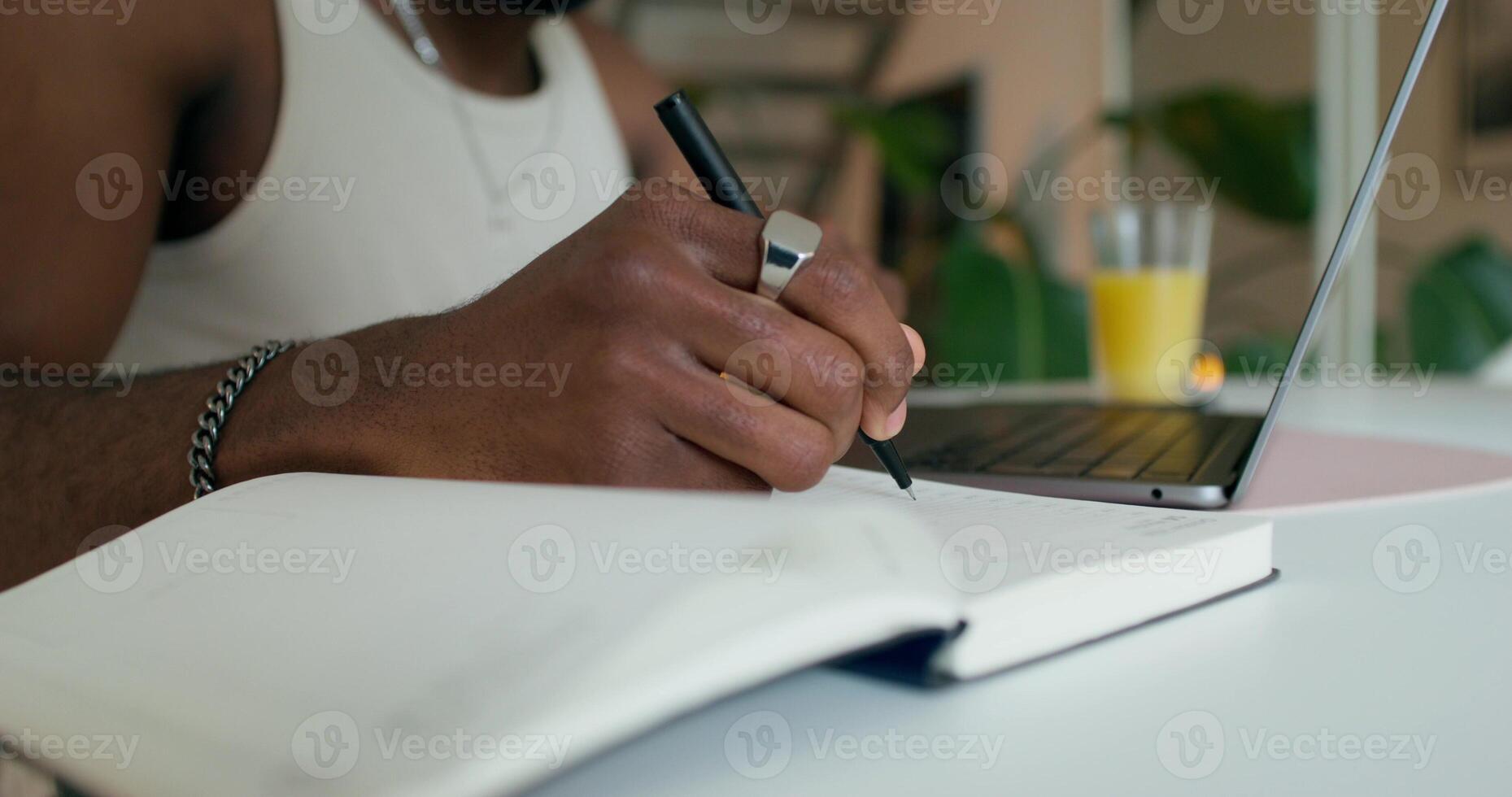 A man uses a laptop and writes in a notebook sitting at a table at home, close-up of his hand, an unrecognizable person photo