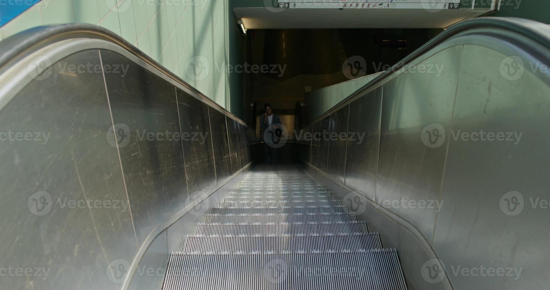 A woman in formal clothes is talking on a mobile phone. She rides the escalator coming up from the subway station - talking photo