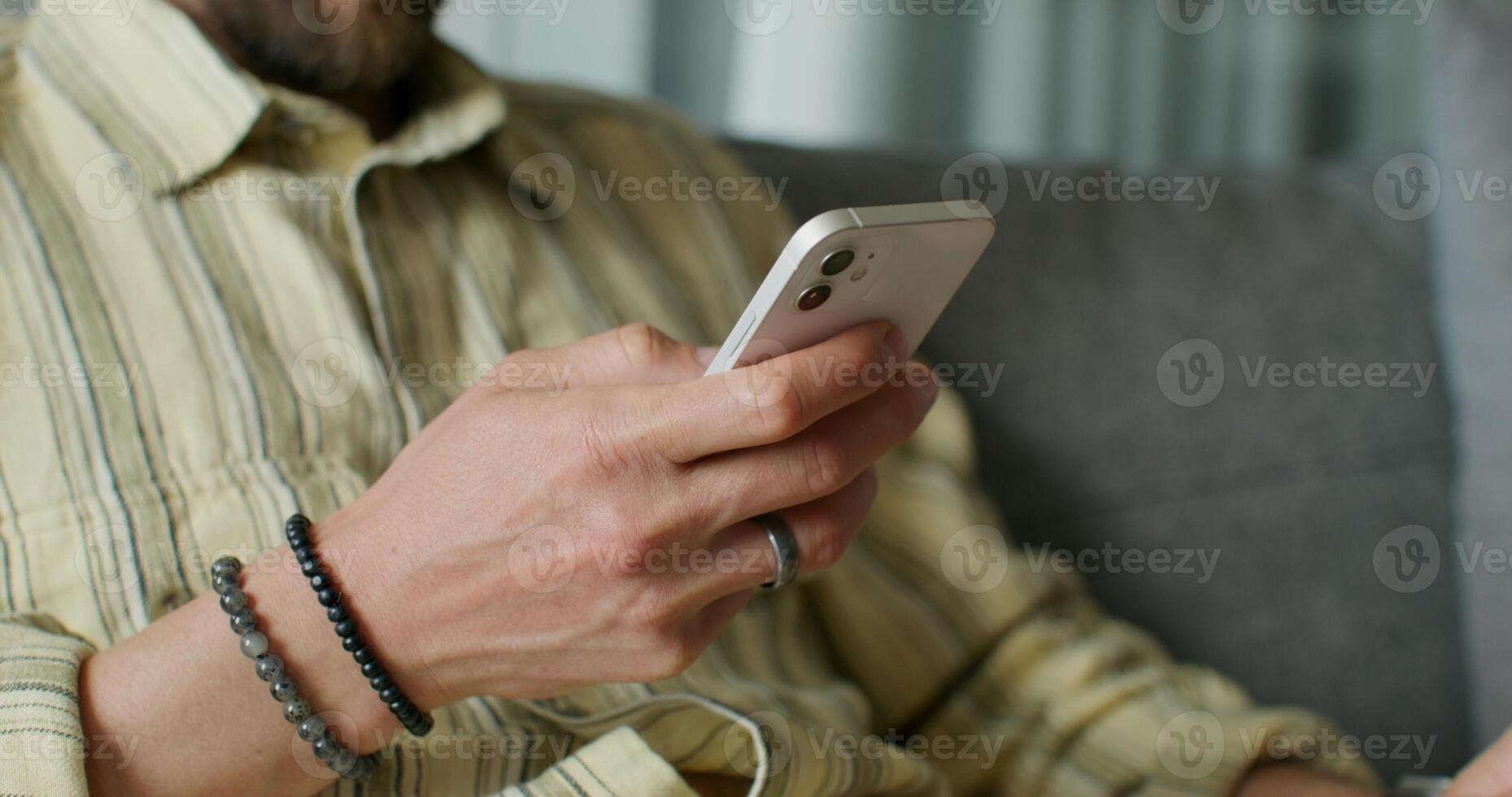 A man is typing on a mobile phone sitting on the couch at home. close-up of his hands, an unrecognizable person. Daylight - unrecognizable photo