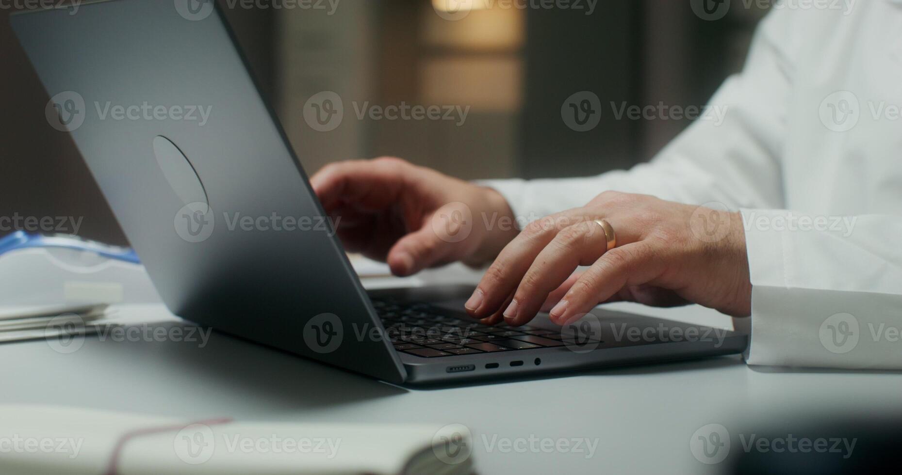 The doctor is typing on a laptop sitting at a table in a medical office, working in a clinic. Close-up of his hands, an unrecognizable person - laptop photo