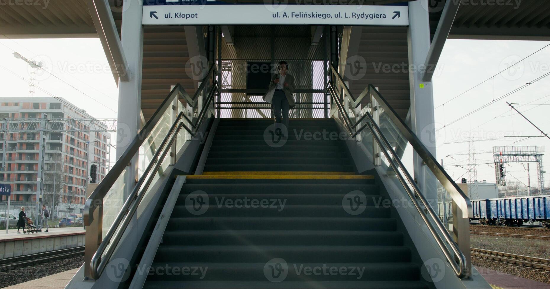 A woman in formal clothes and headphones, with a cup of coffee in her hand, descends the stairs to the platform of the railway station - descends photo