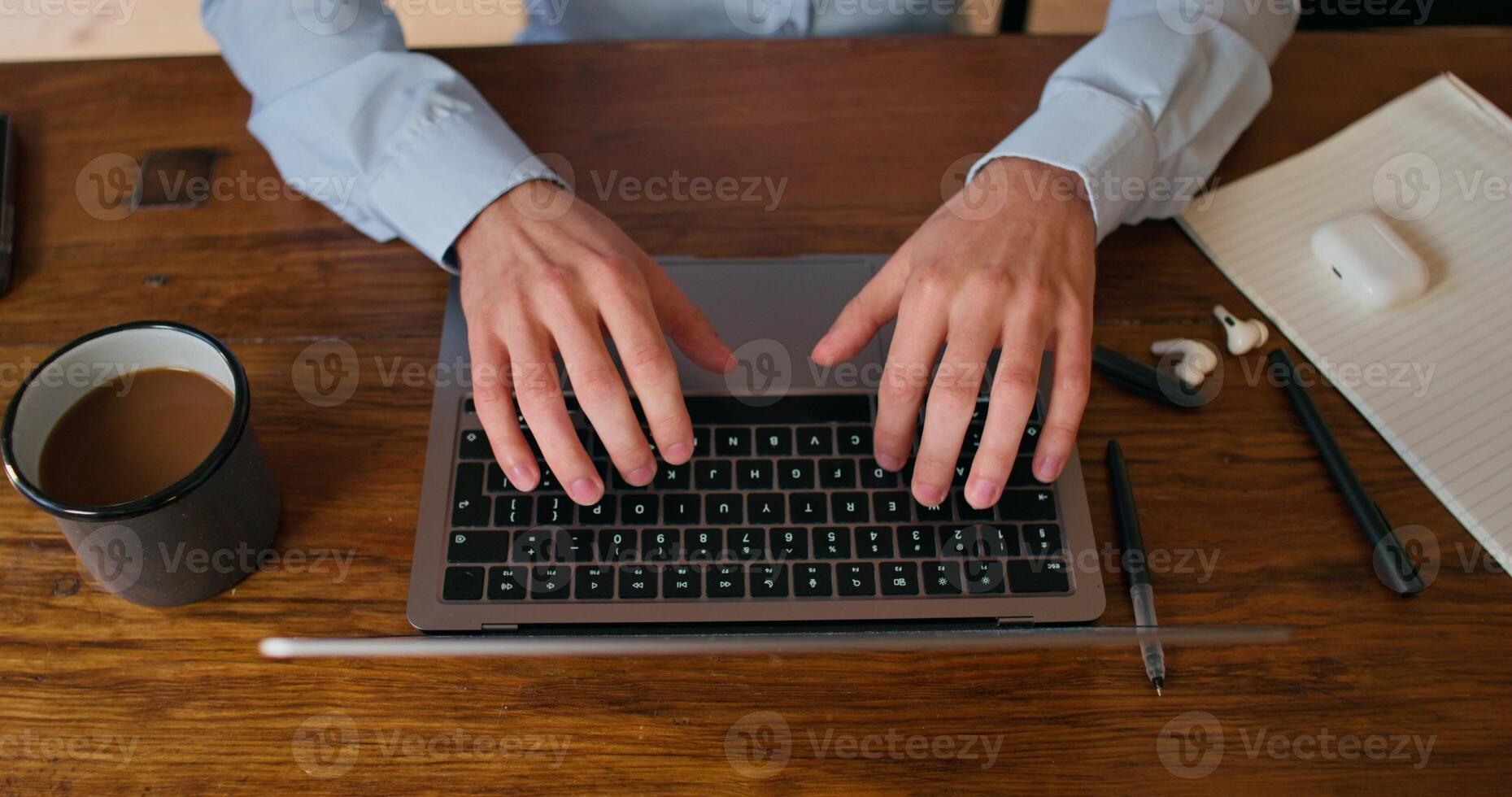 A man uses a laptop and drinks coffee sitting at the kitchen table. Close-up of his hands, an unrecognizable person photo