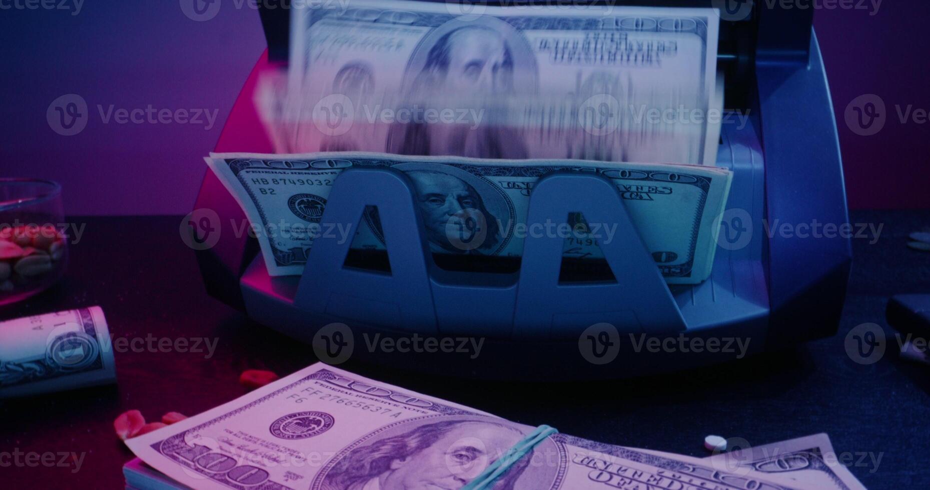 The calculating machine counts hundred dollar bills. Bundles of money are on the table next to a gun, a lighter, an ashtray and other objects - Bundles photo