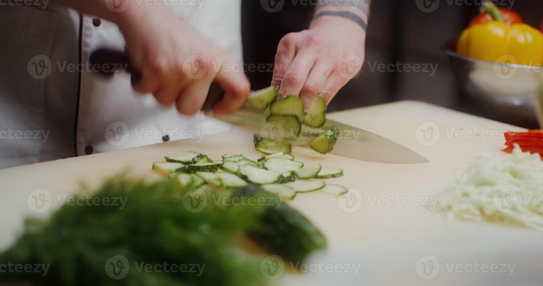 A man in a chef's uniform cuts a cucumber, a close-up of his hands - uniform photo