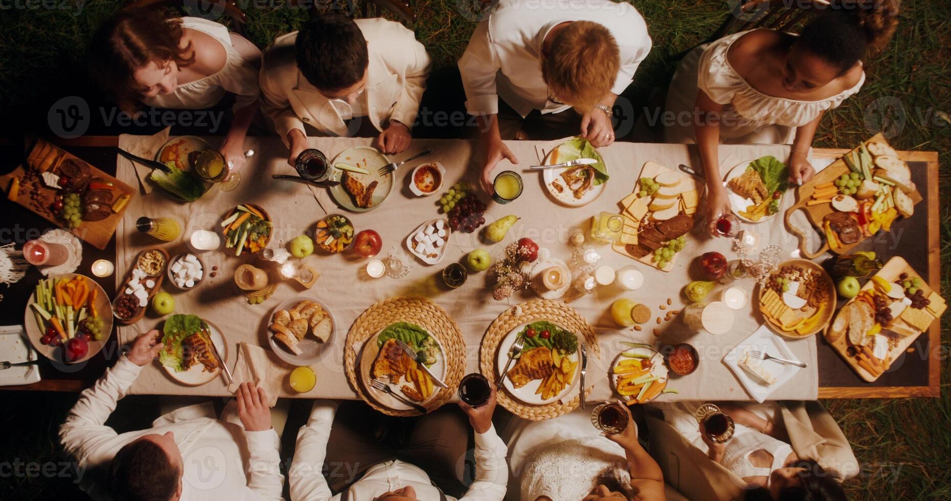 Guests clink glasses sitting at the beautifully served festive table. Top view, outdoor feast photo