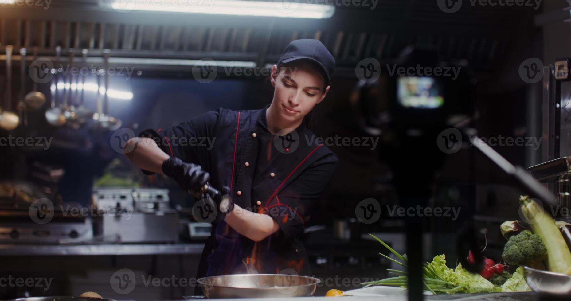 A woman in a chef's uniform talking and smiling recording the cooking process in the restaurant kitchen on camera - process photo