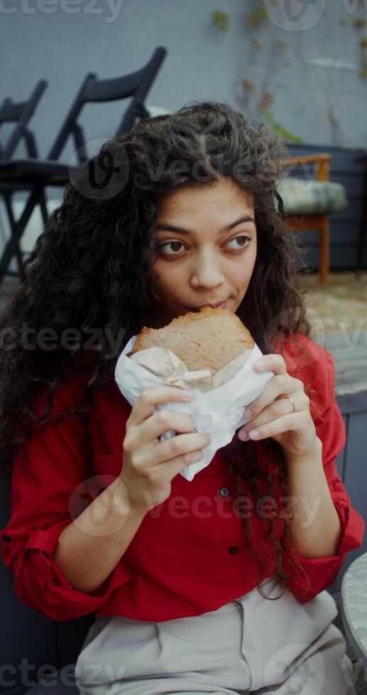 A young woman in casual clothes eats a burger and drinks a mojito while sitting in a cafe - drinks photo