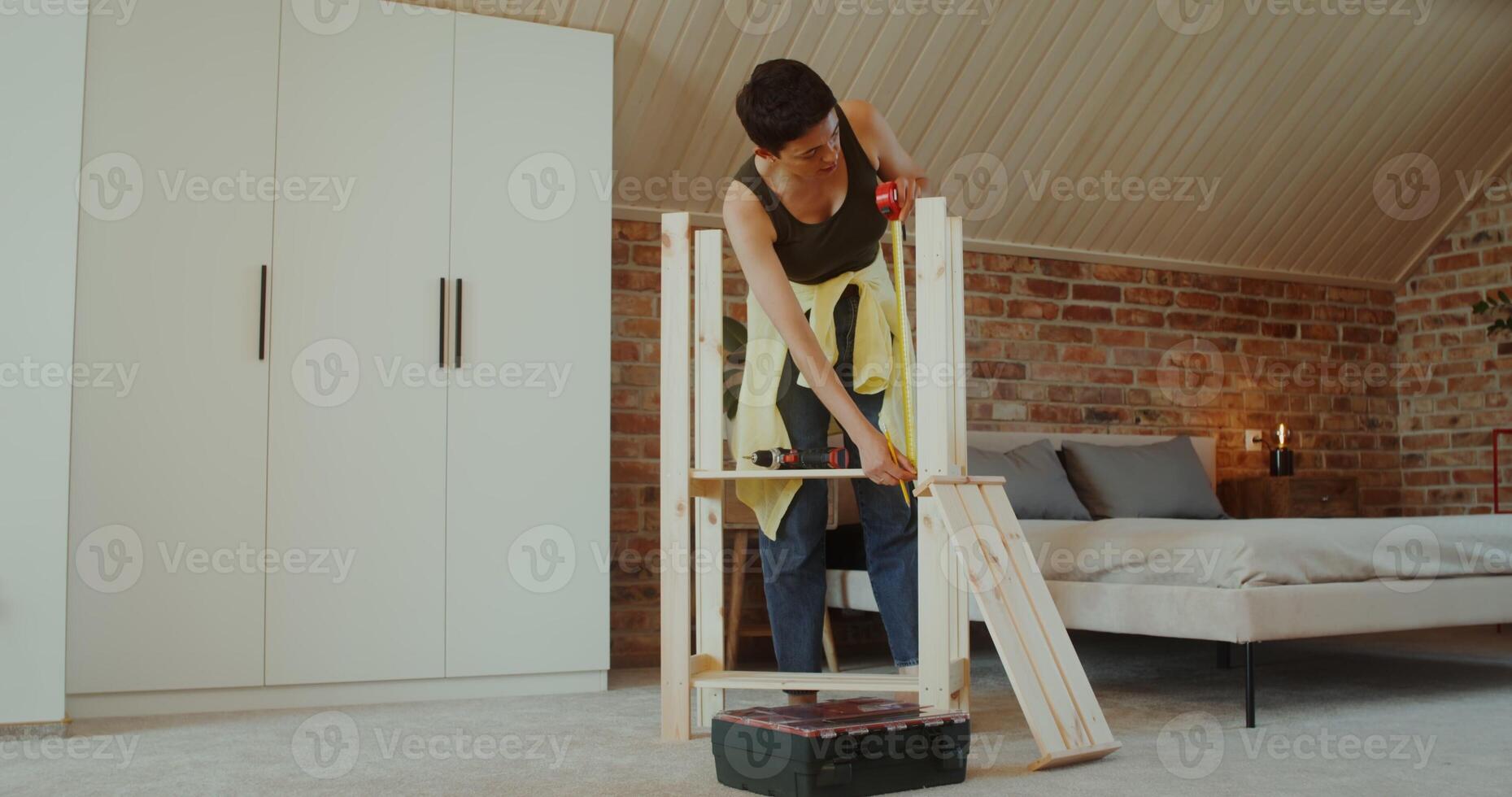 A young woman in casual clothes assembles a rack at home using a tape measure - assembles photo