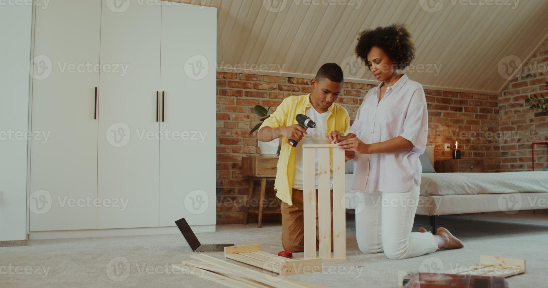 Mom and son make wooden furniture using a drill, sitting on the floor in front of an open laptop at home - laptop photo