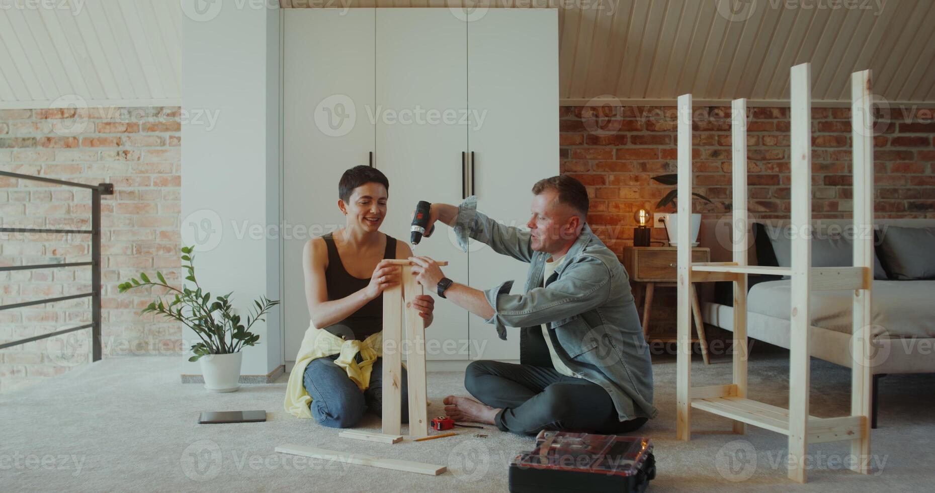 A man and a woman assemble a shelving at home, they use a screwdriver, talk and smile sitting on the floor photo