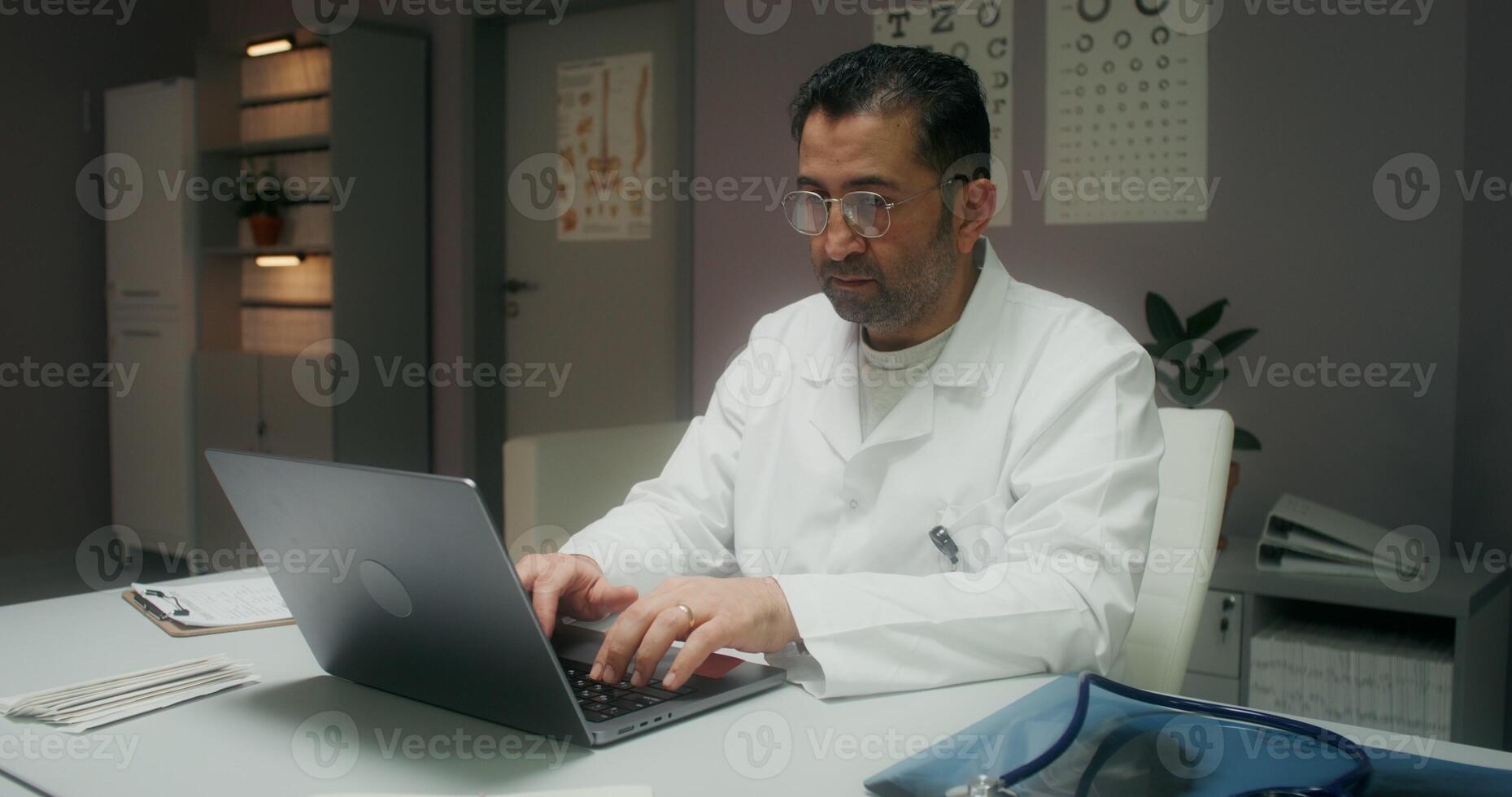 A female patient enters a medical office for a medical appointment. The doctor uses a laptop sitting at the table - enters photo