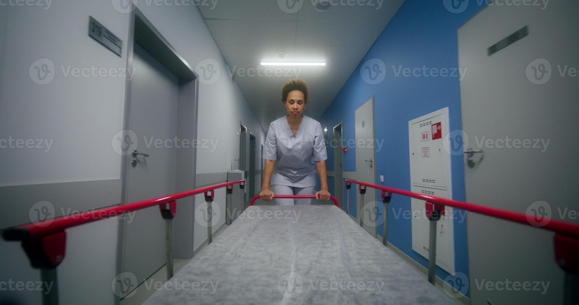 A vie at nurse who carries an empty gurney covered with a disposable sheet down the hospital corridor photo