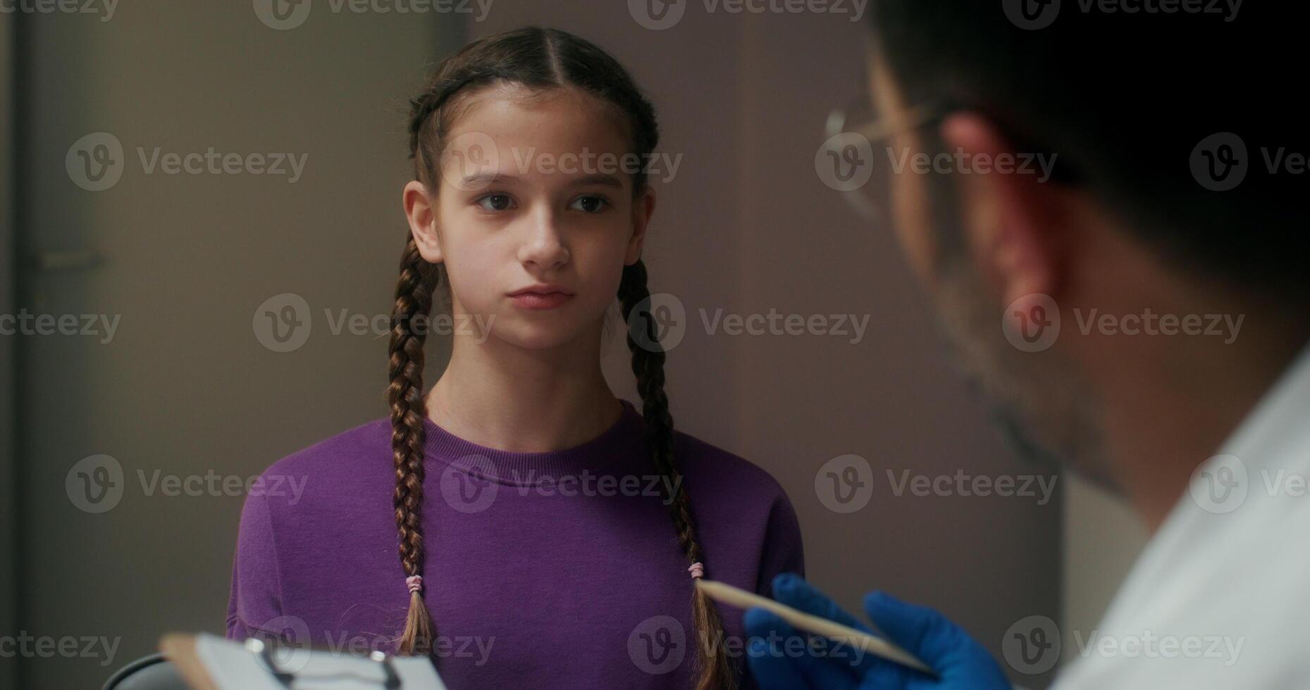 The doctor talks to the girl patient, finding out the symptoms of the disease and writes in a notebook, sitting in the medical office at the clinic - symptoms photo