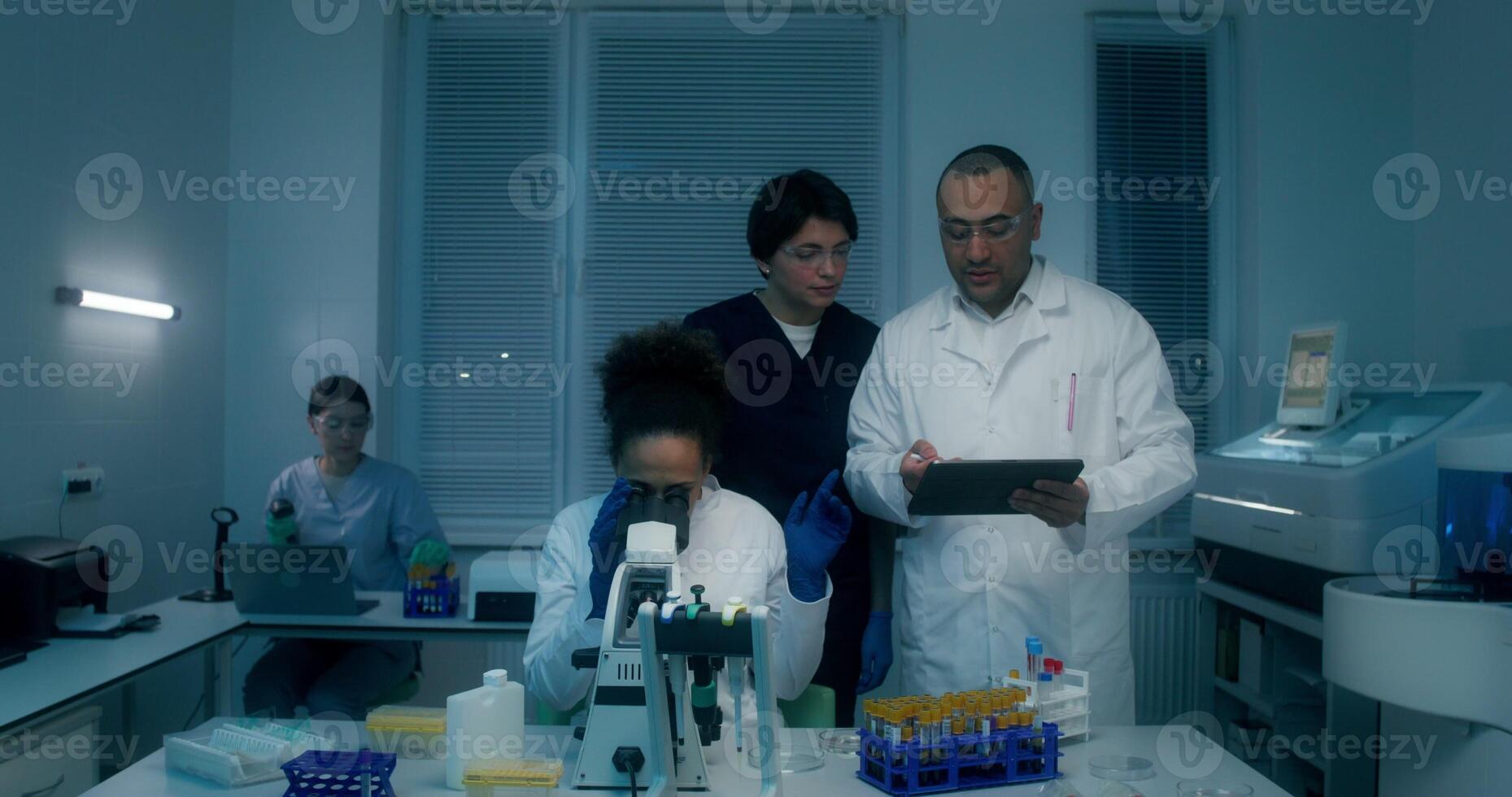 A group of laboratory technicians perform a blood test in the laboratory. A man and a woman use a tablet standing near a laboratory assistant's desk with a microscope - laboratory photo
