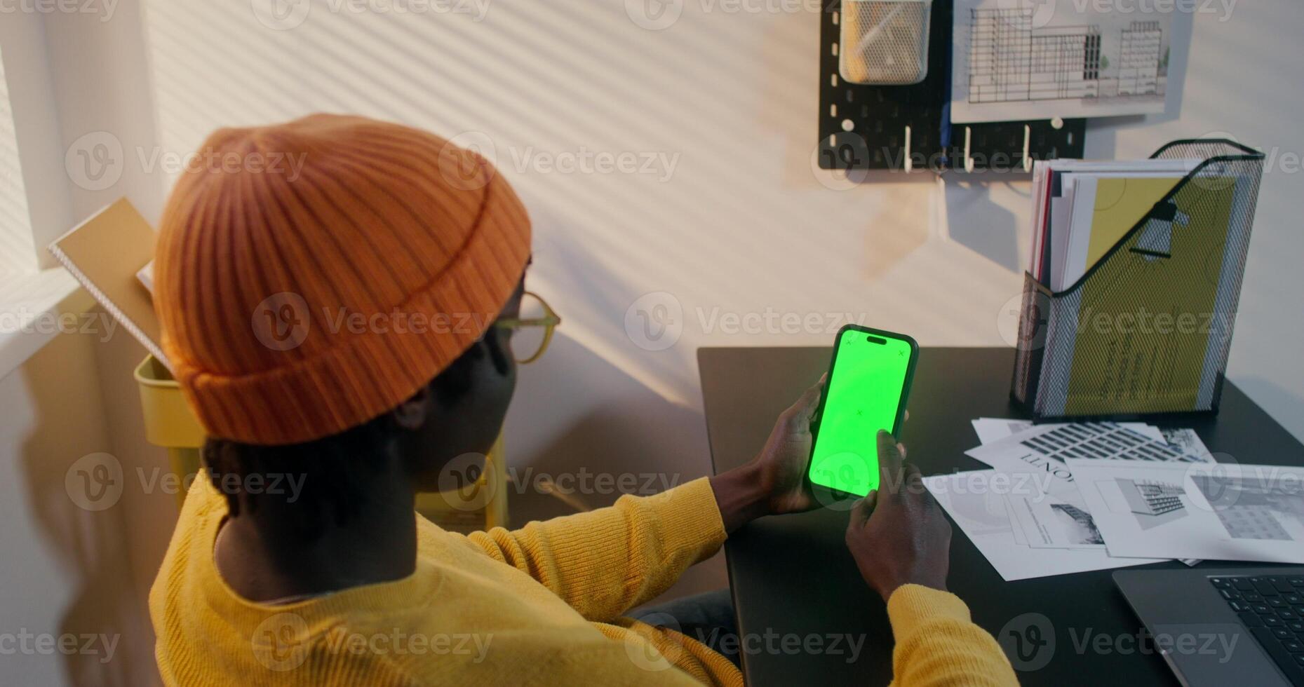 A man in informal clothes uses a mobile phone with green screen sitting at a desk in the office photo