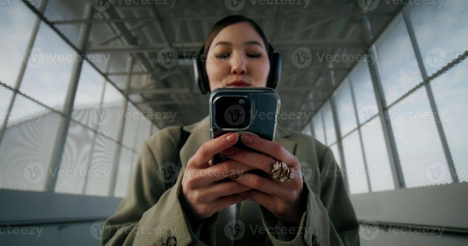 A woman in formal clothes and headphones uses a mobile phone standing in a tunnel, she smiles - headphones photo